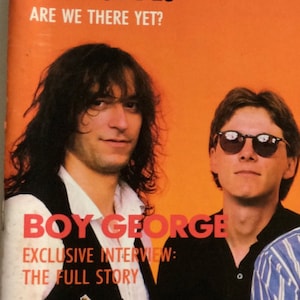 May include: A magazine cover featuring a photo of Boy George, a British singer-songwriter, with the text "Boy George" and "Exclusive Interview: The Full Story" in red letters. The cover also features the text "Are We There Yet?" in white letters.