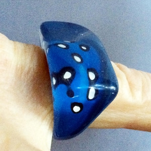 May include: A blue glass ring with white dots. The ring is shaped like a dice and has a rounded edge.