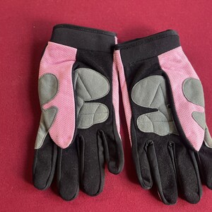 Puede incluir: Un par de guantes negros y rosas con detalles acolchados grises. Los guantes tienen un pu&ntilde;o negro y una tela de malla rosa en el dorso de la mano. La palma y los dedos son negros. Los guantes est&aacute;n dise&ntilde;ados para actividades al aire libre.
