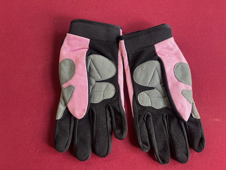 Puede incluir: Un par de guantes negros y rosas con detalles acolchados grises. Los guantes tienen un pu&ntilde;o negro y una tela de malla rosa en el dorso de la mano. La palma y los dedos son negros. Los guantes est&aacute;n dise&ntilde;ados para actividades al aire libre.