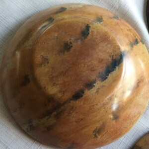 May include: A wooden bowl with a brown and black mottled finish. The bowl is round and has a slight lip around the edge.