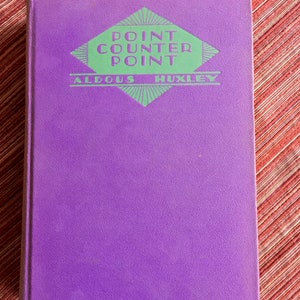 May include: A purple hardcover book with the title "Point Counter Point" by Aldous Huxley printed in green on the front cover.