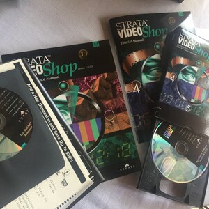 Pu&ograve; includere: Una collezione di manuali software e un CD per il programma Strata VideoShop. I manuali sono neri con testo verde e bianco. Il CD &egrave; in una custodia nera con un disco argentato. Il testo sui manuali include "Strata VideoShop", "Manuale del tutorial", "Manuale di riferimento", "Aggiungi una nuova dimensione e risparmia fino a 300 &euro;!" e "3D".