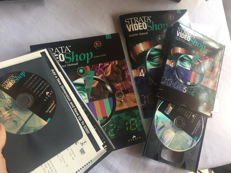 Pu&ograve; includere: Una collezione di manuali software e un CD per il programma Strata VideoShop. I manuali sono neri con testo verde e bianco. Il CD &egrave; in una custodia nera con un disco argentato. Il testo sui manuali include "Strata VideoShop", "Manuale del tutorial", "Manuale di riferimento", "Aggiungi una nuova dimensione e risparmia fino a 300 &euro;!" e "3D".