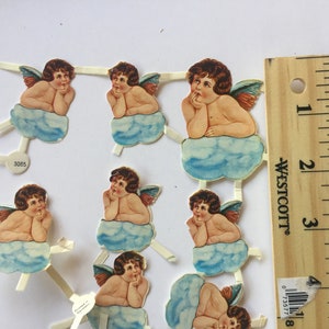 May include: Nine vintage paper angel cutouts with blue clouds and wings. The angels are all in a thinking pose with their hands on their chins. The cutouts are on a white background with a ruler for scale.