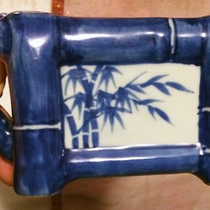 May include: Blue and white ceramic teapot with a bamboo design. The teapot has a handle and a spout. The design features a white background with blue bamboo stalks and leaves.