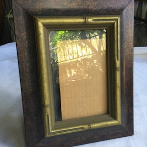 Może przedstawiać: Brązowa ramka do zdjęć z pozłacanym wewnętrznym obramowaniem. Ramka ma postarzony wygląd i jest wykonana z drewna. Ramka jest pusta i gotowa do włożenia zdjęcia.