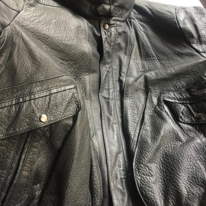 Pu&ograve; includere: Una giacca bomber in pelle nera con chiusura a zip e due tasche. La giacca ha un colletto a stand-up e un orlo a costine.