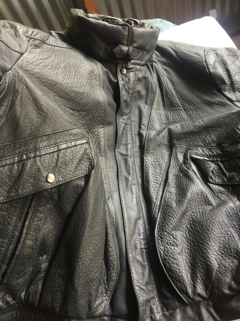 Pu&ograve; includere: Una giacca bomber in pelle nera con chiusura a zip e due tasche. La giacca ha un colletto a stand-up e un orlo a costine.