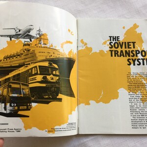May include: A vintage book cover with a yellow map of the Soviet Union and a collage of transportation vehicles including a plane, a ship, a train, and a bus. The text on the cover reads "The Soviet Transport System".