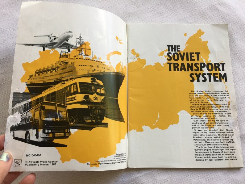 May include: A vintage book cover with a yellow map of the Soviet Union and a collage of transportation vehicles including a plane, a ship, a train, and a bus. The text on the cover reads "The Soviet Transport System".