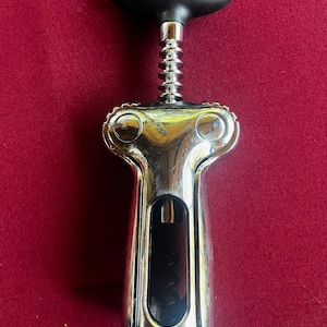 May include: A silver wine opener with a black rubber handle. The opener has a lever and a corkscrew.
