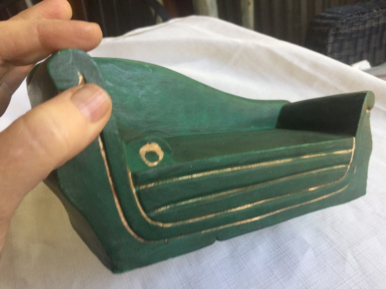 May include: A miniature green couch with gold trim. The couch is made of wood and has a simple, elegant design.