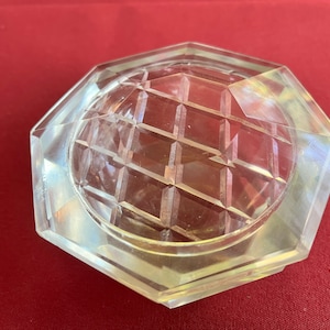 Op de afbeelding: Een doorzichtig, achthoekig glazen deksel met een geometrisch patroon. Het deksel is ontworpen om op een pot of container te passen.