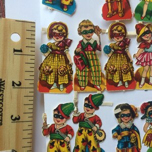 Peut inclure: Un ensemble de poup&eacute;es en papier vintage avec des costumes et des masques color&eacute;s. Les poup&eacute;es sont habill&eacute;es de diff&eacute;rentes tenues, dont une robe jaune, un costume &agrave; carreaux et une robe rose. Les poup&eacute;es portent toutes des masques avec des motifs diff&eacute;rents.