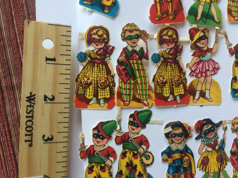 Peut inclure: Un ensemble de poup&eacute;es en papier vintage avec des costumes et des masques color&eacute;s. Les poup&eacute;es sont habill&eacute;es de diff&eacute;rentes tenues, dont une robe jaune, un costume &agrave; carreaux et une robe rose. Les poup&eacute;es portent toutes des masques avec des motifs diff&eacute;rents.