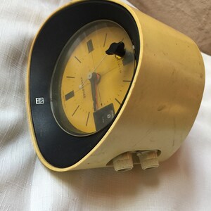 May include: A yellow vintage Panasonic alarm clock with a black face and a white dial. The clock has a round shape and two knobs on the side.