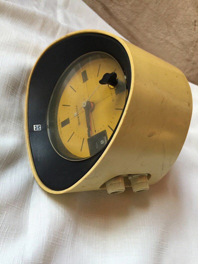 May include: A yellow vintage Panasonic alarm clock with a black face and a white dial. The clock has a round shape and two knobs on the side.