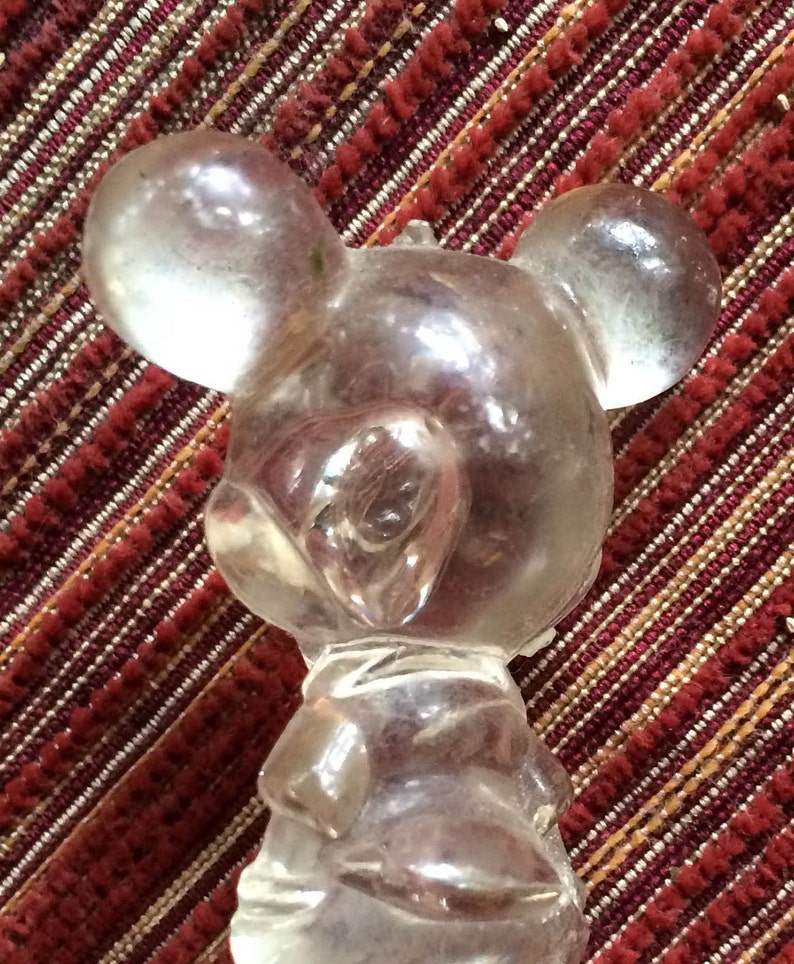 Puede incluir: Una figurita de pl&aacute;stico transparente de Mickey Mouse. La figurita est&aacute; de pie con los brazos a los lados. La figurita es un juguete vintage.