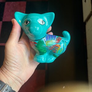 May include: A turquoise ceramic figurine of a dog with colorful painted details. The dog has large eyes and a playful expression.