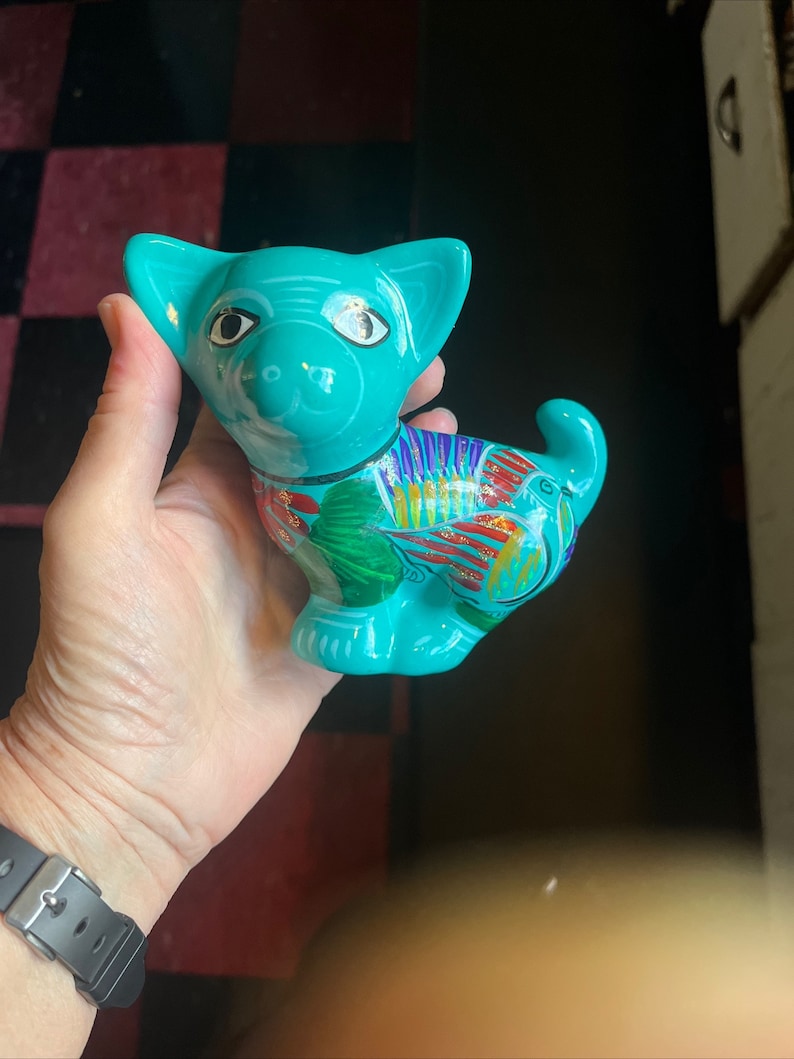 May include: A turquoise ceramic figurine of a dog with colorful painted details. The dog has large eyes and a playful expression.