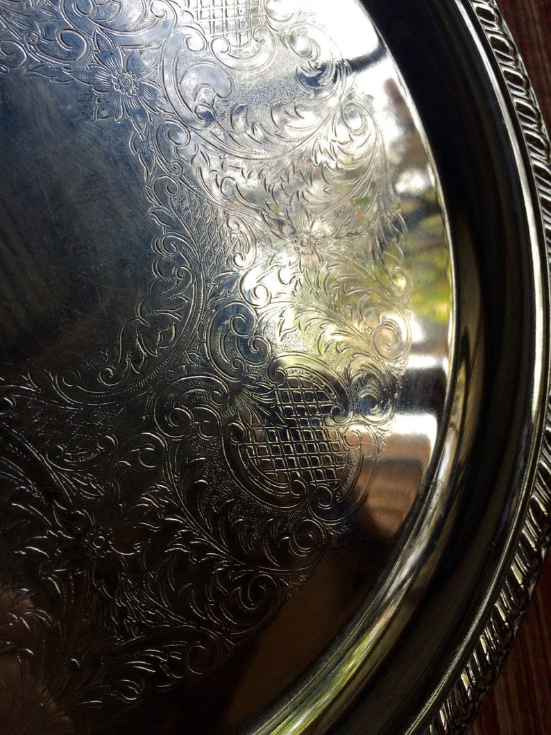 May include: A silver serving tray with an ornate, embossed design. The tray has a raised rim and a smooth, reflective surface.