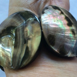 May include: A pair of large, round, iridescent shell bracelets. The shells are a dark brown colour with green and purple iridescent highlights.