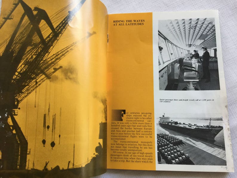 May include: A vintage book with a yellow cover and black text. The text reads "Riding the Waves at All Latitudes". The book is open to a page with a black and white photo of a ship's bridge and a photo of a large ship in the water.