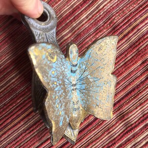 May include: A vintage metal butterfly-shaped object with a handle. The butterfly has blue and gold paint with black details. The handle is a light gray color with decorative detailing.