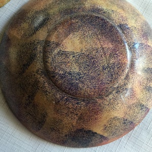 May include: A wooden bowl with a speckled, multi-colored finish. The bowl has a dark brown, purple, and yellow color scheme. The bowl is round and has a slight lip around the edge.
