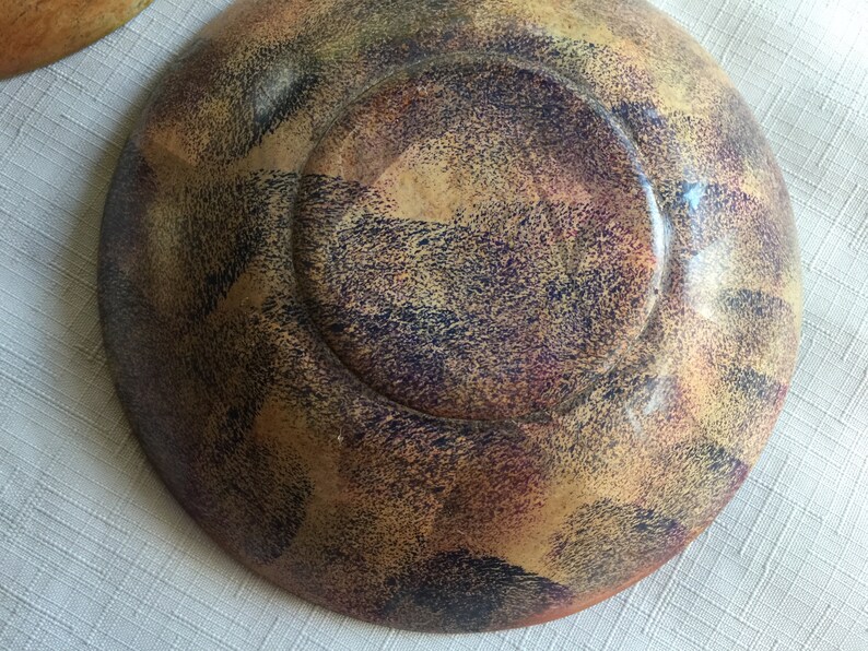 May include: A wooden bowl with a speckled, multi-colored finish. The bowl has a dark brown, purple, and yellow color scheme. The bowl is round and has a slight lip around the edge.