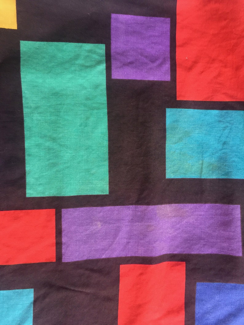 K&ouml;nnte beinhalten: Ein schwarzer Stoff mit einem geometrischen Muster aus bunten Quadraten. Die Quadrate sind in den Farben Rot, Lila, Gr&uuml;n, Blau und Gelb.
