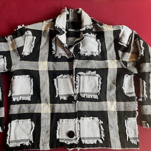 May include: A black and white checkered jacket with frayed edges and white squares that have a woven texture. The jacket has a button closure and long sleeves.