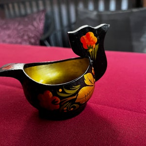 May include: A small black wooden bird-shaped cup with a gold interior. The cup is decorated with traditional Russian folk art, featuring red, yellow, and green floral designs.