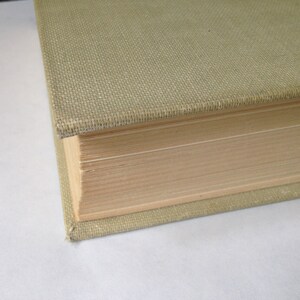May include: Close-up of the spine of a hardcover book with a light green fabric cover. The pages are visible and the book is closed.