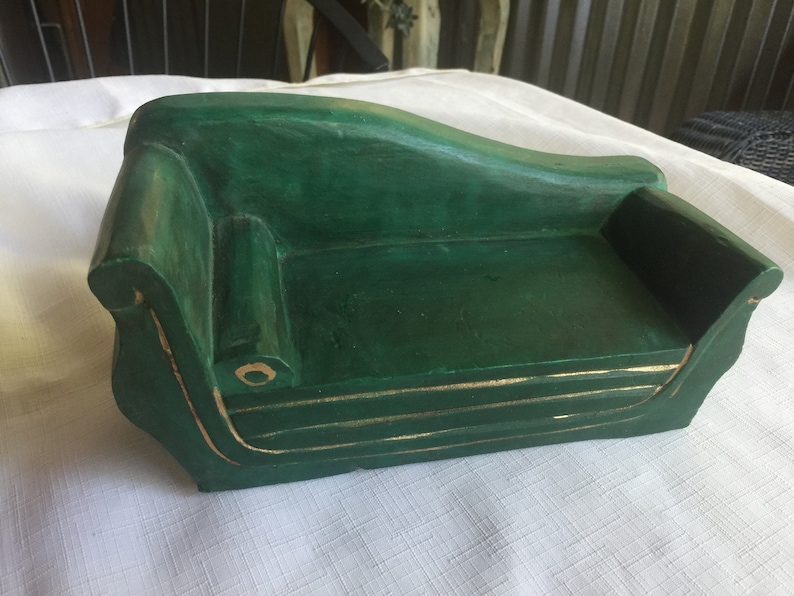 May include: A small, green wooden sofa with gold trim. The sofa is a miniature version of a traditional sofa and would be perfect for a dollhouse or other miniature setting.