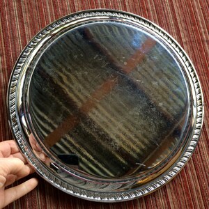 May include: A silver serving tray with a raised, decorative rim. The tray is round and has a shiny, reflective surface.