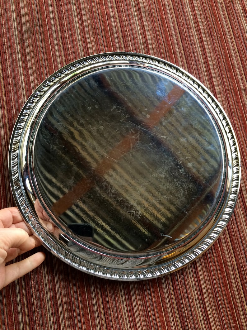 May include: A silver serving tray with a raised, decorative rim. The tray is round and has a shiny, reflective surface.