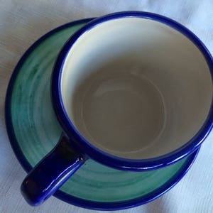 May include: A blue and green ceramic teacup and saucer set. The cup has a white interior and a blue rim. The saucer has a green and blue swirl design.
