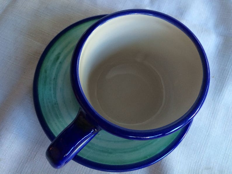 May include: A blue and green ceramic teacup and saucer set. The cup has a white interior and a blue rim. The saucer has a green and blue swirl design.