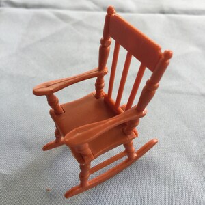 K&ouml;nnte beinhalten: Ein kleiner, brauner Schaukelstuhl aus Plastik. Der Stuhl hat eine abgerundete R&uuml;ckenlehne und eine leicht gew&ouml;lbte Sitzfl&auml;che. Die Schaukelbasis besteht aus einem einzigen St&uuml;ck Plastik.