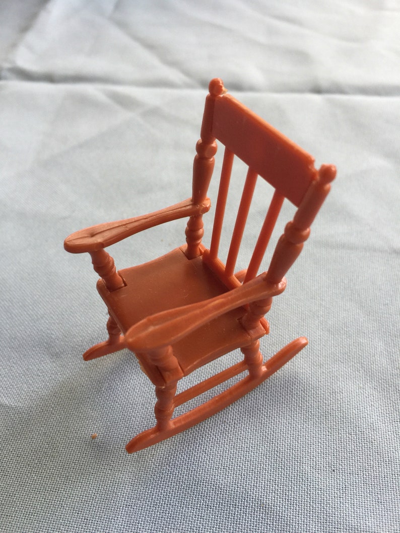 K&ouml;nnte beinhalten: Ein kleiner, brauner Schaukelstuhl aus Plastik. Der Stuhl hat eine abgerundete R&uuml;ckenlehne und eine leicht gew&ouml;lbte Sitzfl&auml;che. Die Schaukelbasis besteht aus einem einzigen St&uuml;ck Plastik.