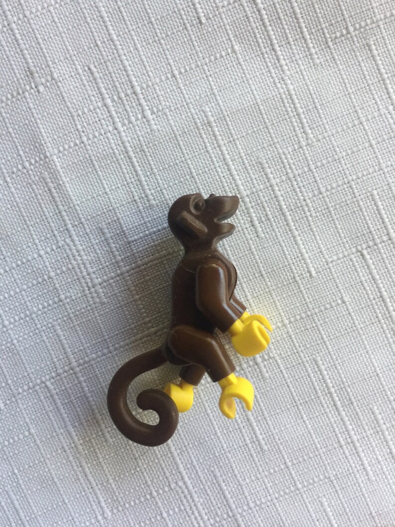 May include: A brown plastic monkey figurine with yellow hands and feet. The monkey is sitting with its tail curled behind it.