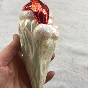 以下が含まれることがあります： サンタクロースの形をしたクリスマスオーナメント。オーナメントは、白いグリッタートリムが付いた赤い帽子、白いひげ、真珠色のボディが特徴です。オーナメントは手で持たれています。