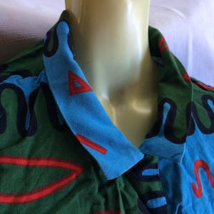 K&ouml;nnte beinhalten: Ein Hemd mit einem blauen, gr&uuml;nen und roten Muster. Das Muster zeigt wellenf&ouml;rmige Linien und geometrische Formen.