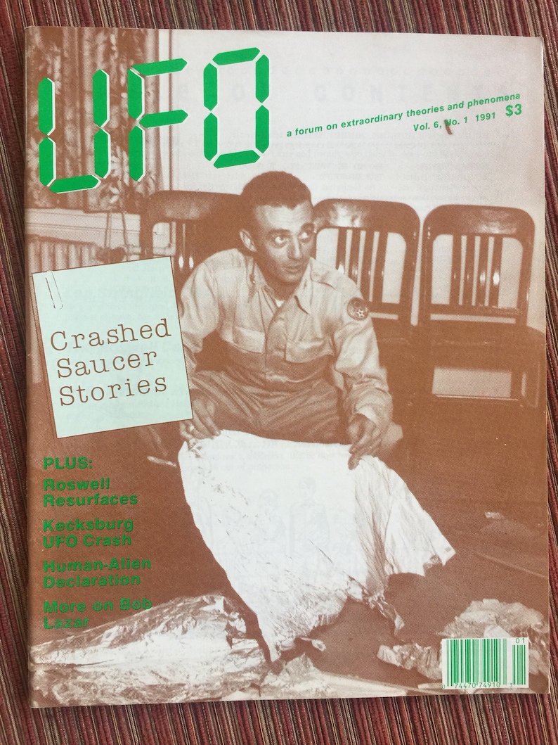 Puede incluir: Un n&uacute;mero de 1991 de la revista UFO, volumen 6, n&uacute;mero 1, con una fotograf&iacute;a de portada en tono sepia de una persona examinando restos met&aacute;licos. La portada incluye el texto UFO, Crashed Saucer Stories, Roswell Resurfaces, Kecksburg UFO Crash y Human-Alien Declaration.