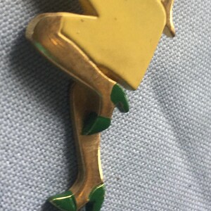 Puede incluir: Figurita de metal dorado de una mujer con un vestido amarillo y zapatos verdes. La figurita est&aacute; en posici&oacute;n sentada con una pierna doblada y la otra extendida.