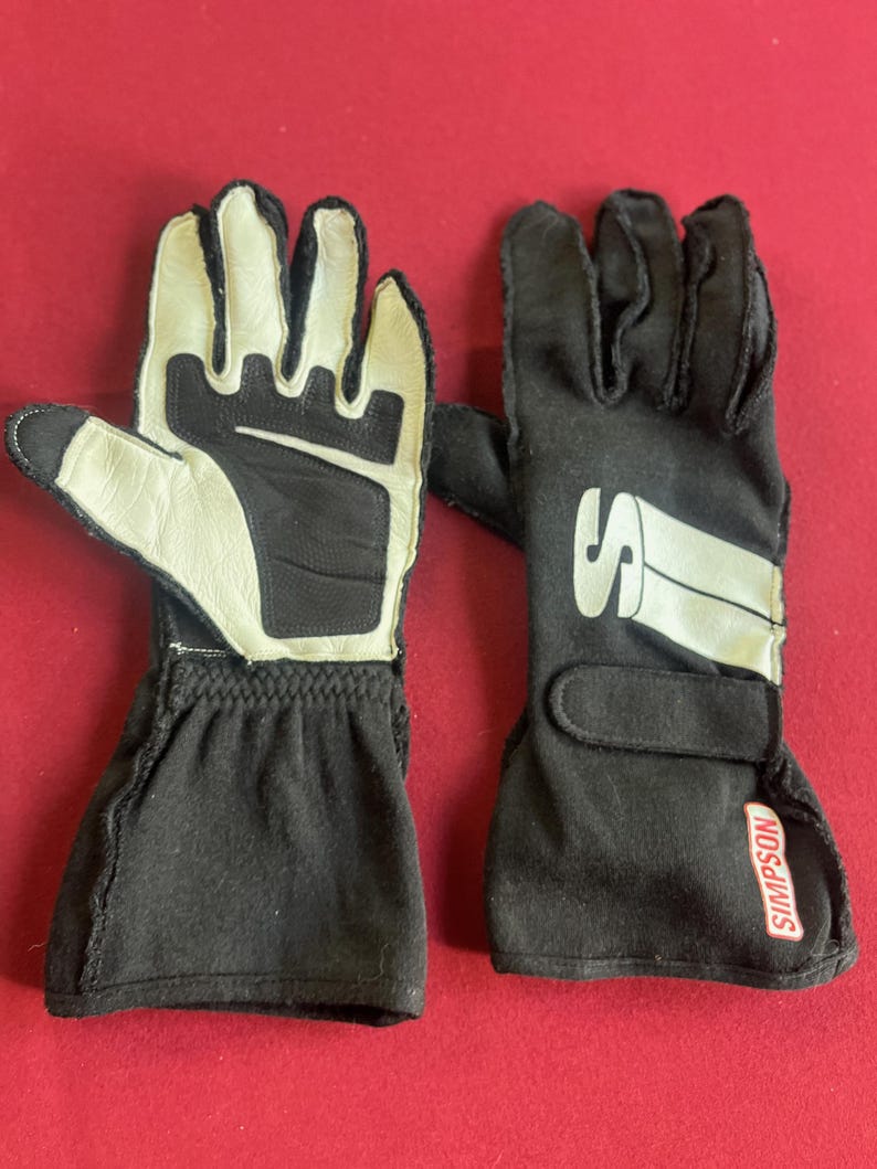 Puede incluir: Un par de guantes de carreras en blanco y negro. Los guantes tienen un pu&ntilde;o negro y una zona de palma y dedos blanca. La marca "SIMPSON" es visible en la correa de la mu&ntilde;eca.