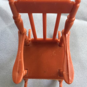 K&ouml;nnte beinhalten: Ein brauner Plastik-Schaukelstuhl mit schlichtem Design. Der Stuhl hat eine hohe R&uuml;ckenlehne und geschwungene Armlehnen. Der Stuhl besteht aus einem einzigen St&uuml;ck Plastik und hat eine glatte Oberfl&auml;che.