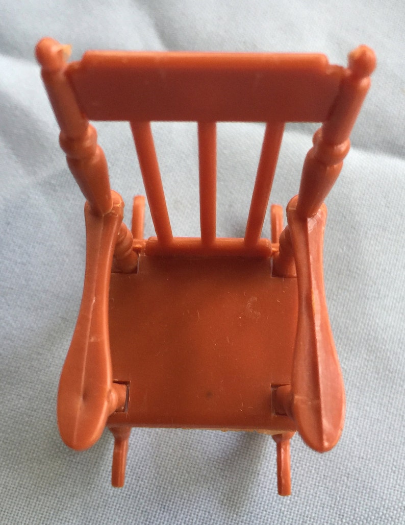 K&ouml;nnte beinhalten: Ein brauner Plastik-Schaukelstuhl mit schlichtem Design. Der Stuhl hat eine hohe R&uuml;ckenlehne und geschwungene Armlehnen. Der Stuhl besteht aus einem einzigen St&uuml;ck Plastik und hat eine glatte Oberfl&auml;che.
